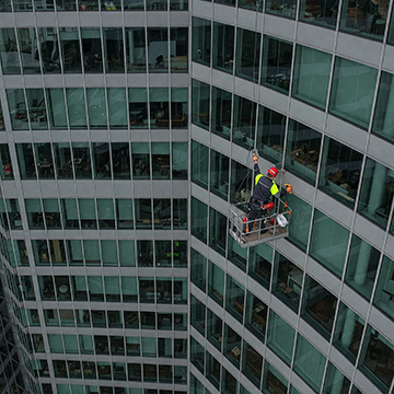 A maintenance technician conducts preventive maintenance on the outside of a large facility.