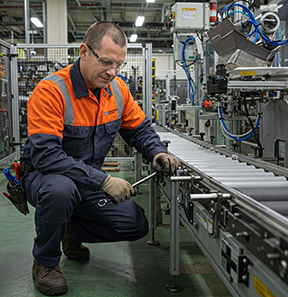 A technician conducts preventive maintenance on a conveyor belt to prevent manufacturing errors.